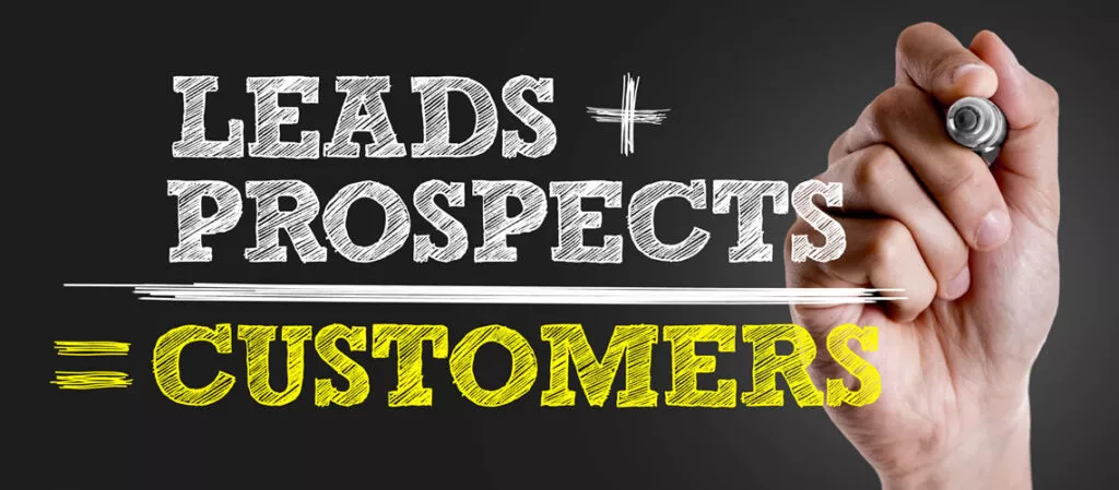 Hand writing the sales formula “Leads + Prospects = Customers” on a blackboard-style background for sales prospecting.