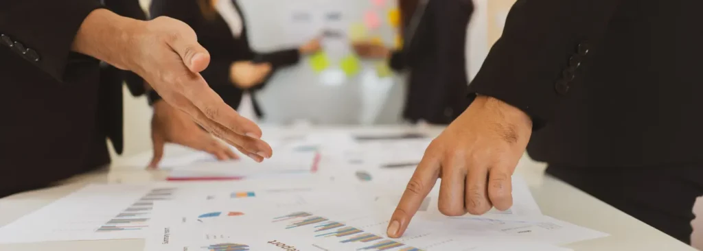 Close-up of businesspeople’s hands pointing at sales reports and charts during a meeting.