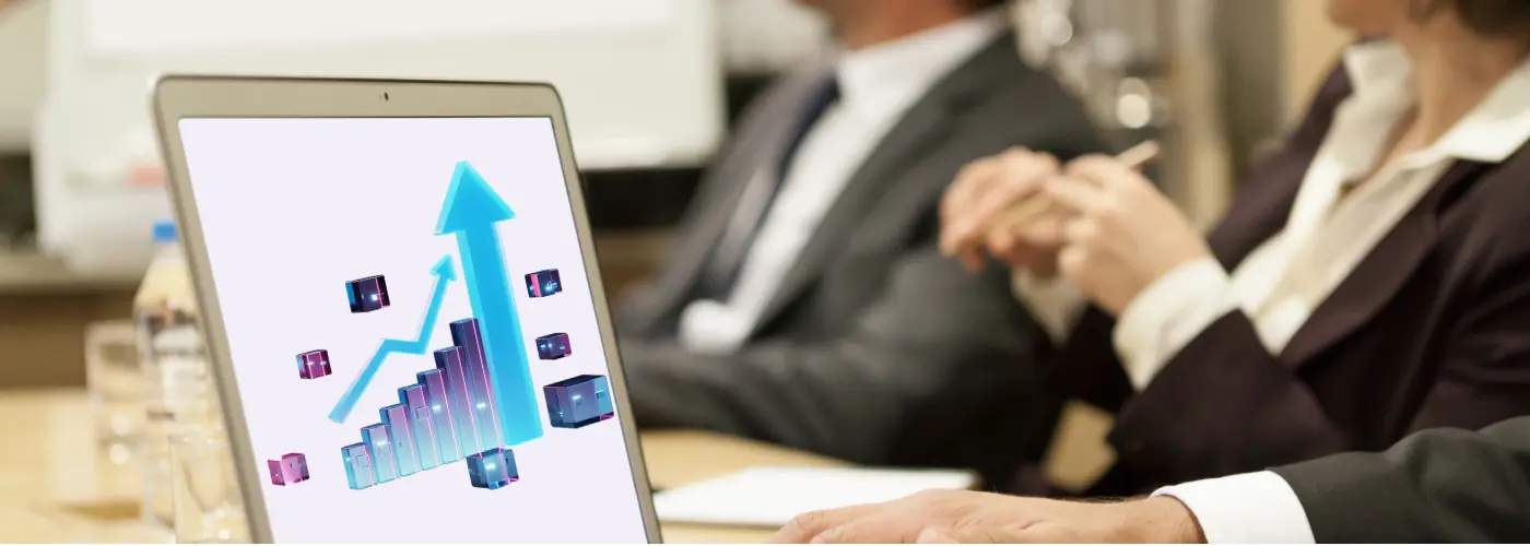 Laptop screen showing an upward sales graph in a meeting with businesspeople, illustrating sales prospecting numbers and pipeline growth.
