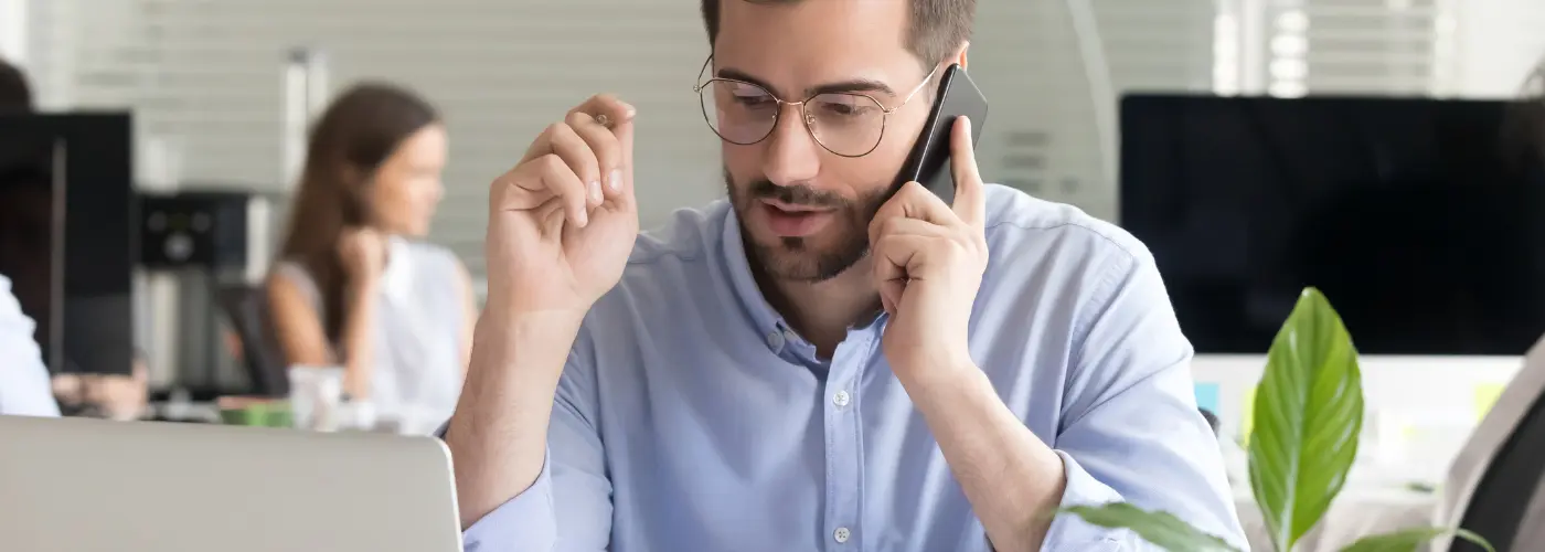 Sales professional making a phone prospecting call at a desk with notes and laptop in front of them.