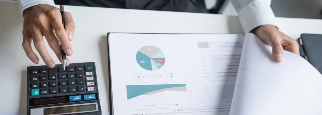 Business professional using a calculator and reviewing pie charts and graphs on a report, calculating the business case for a Challenger sales play..