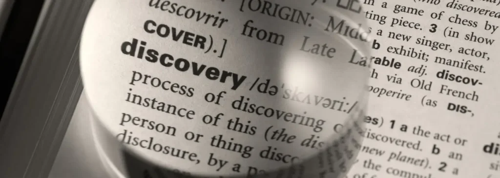Close-up of the word discovery under a magnifying glass in a dictionary, symbolizing focused sales discovery questions in selling