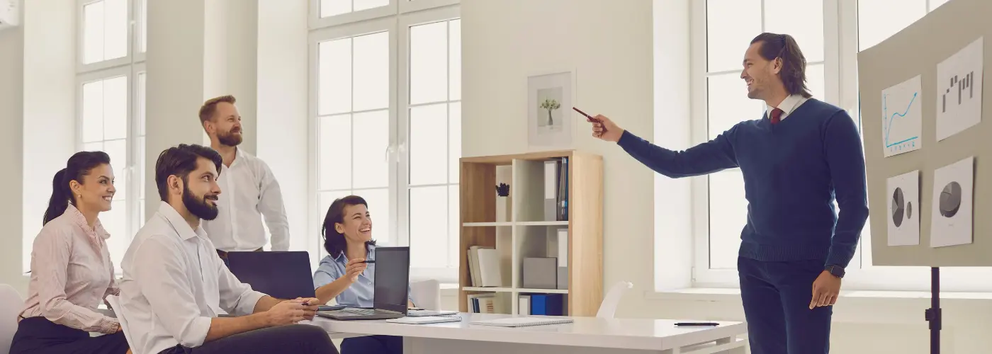 Sales manager coaching a team beside a whiteboard showing a pipeline dashboard